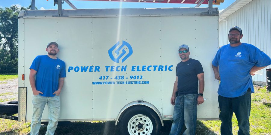 Three electricians standing in front of a branded work trailer, representing the skilled team behind reliable electrical services.