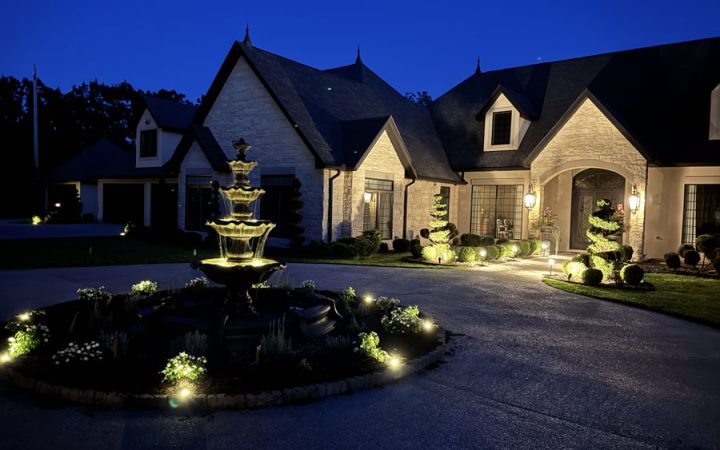 A beautifully lit home exterior with warm lighting around the entrance and landscaping, demonstrating expert residential lighting design.
