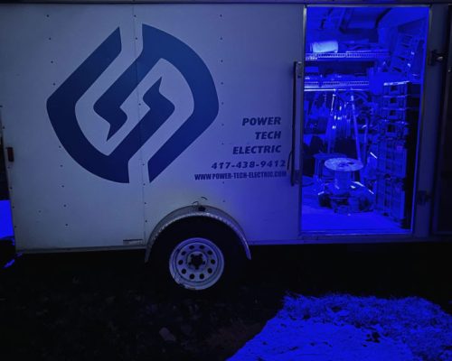 A branded work trailer equipped with tools and supplies, illuminated at night, ready for emergency or routine electrical services.