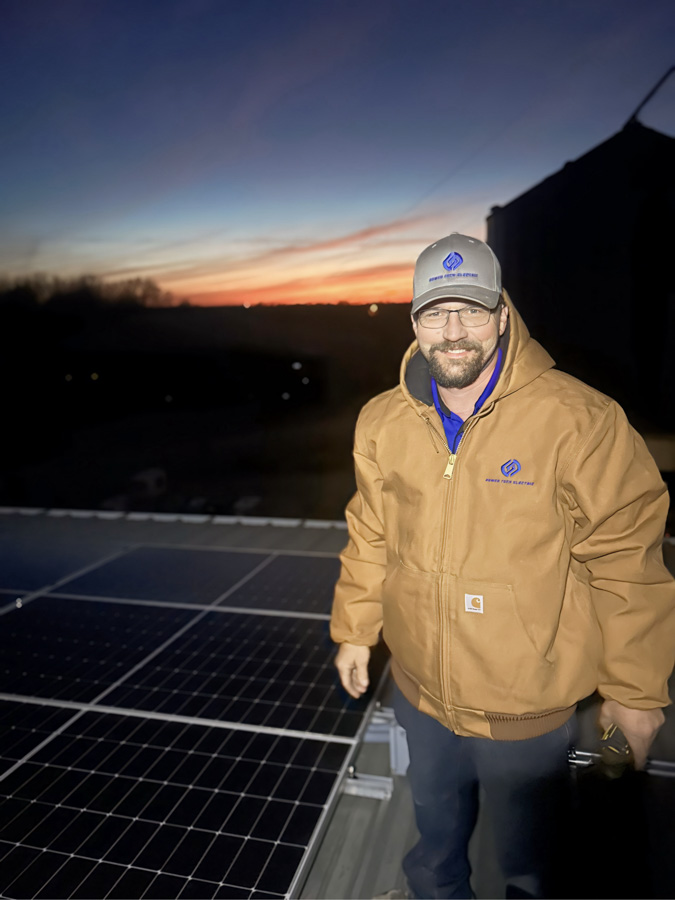 An electrician standing on a roof with installed solar panels, highlighting expertise in solar energy solutions.